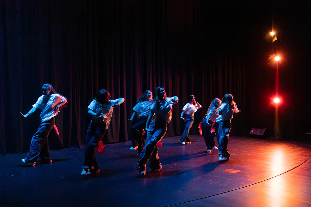 Sieben Tänzerinnen bewegen sich synchron in blau-rotem Licht.